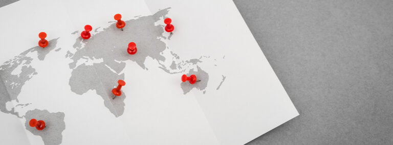 A simple map of the world with red pinboard pins charting the international expansion of a company.
