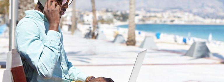 A man on a working holiday, sitting on a bench next to the beach with his laptop open and talking on his mobile phone. Culture trip PR coverage and links case study